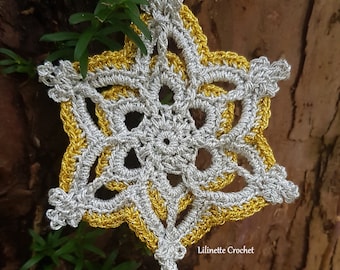 Op de afbeelding: Een zilveren en gouden gehaakte sneeuwvlok ornament met een gouden kralen druppel die eraan hangt. De ornament hangt aan een tak.