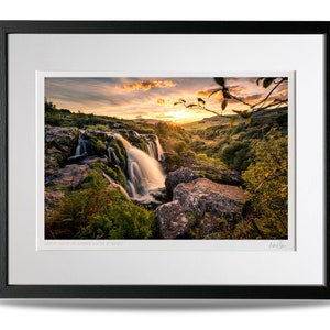 Puede incluir: Una fotograf&iacute;a enmarcada de una cascada que cae sobre rocas con una puesta de sol en el fondo. La imagen se titula "Last of Light at the Sgwd Gwladys Water at Sunset".
