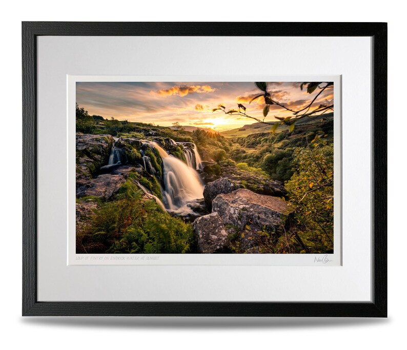 Puede incluir: Una fotograf&iacute;a enmarcada de una cascada que cae sobre rocas con una puesta de sol en el fondo. La imagen se titula "Last of Light at the Sgwd Gwladys Water at Sunset".