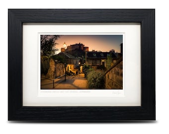 May include: A photograph of Edinburgh Castle and the Vennel, Edinburgh, Scotland. The castle is lit up in the distance, and the street below is lined with buildings. The photo is taken at dusk, and the sky is a soft orange and purple.