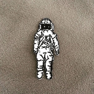 Op de afbeelding: Zwart-witte geborduurde patch van een astronaut met helm en ruimtepak.