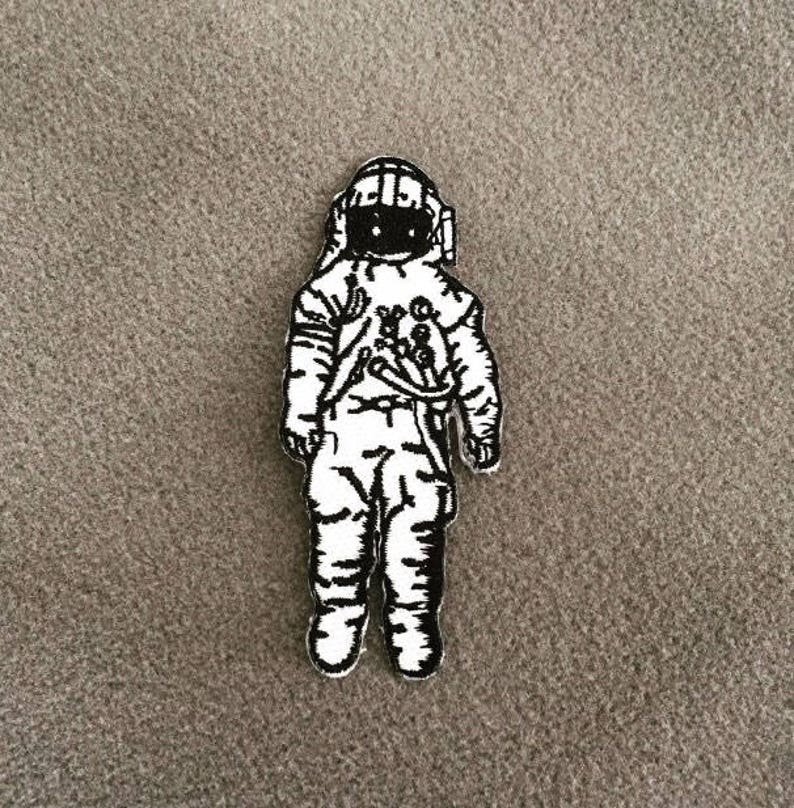 Op de afbeelding: Zwart-witte geborduurde patch van een astronaut met helm en ruimtepak.