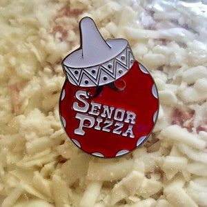 May include: A red and white enamel pin with the words "Senor Pizza" in white lettering. The pin is shaped like a sombrero.