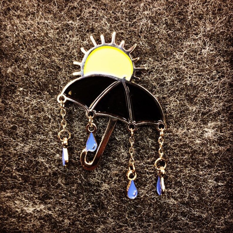 May include: A black umbrella with a yellow sun on top and gold chains with blue raindrops hanging from the bottom.