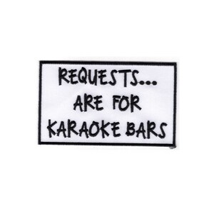 K&ouml;nnte beinhalten: Wei&szlig;er rechteckiger Patch mit schwarzem gesticktem Text, der "REQUESTS... ARE FOR KARAOKE BARS" lautet.