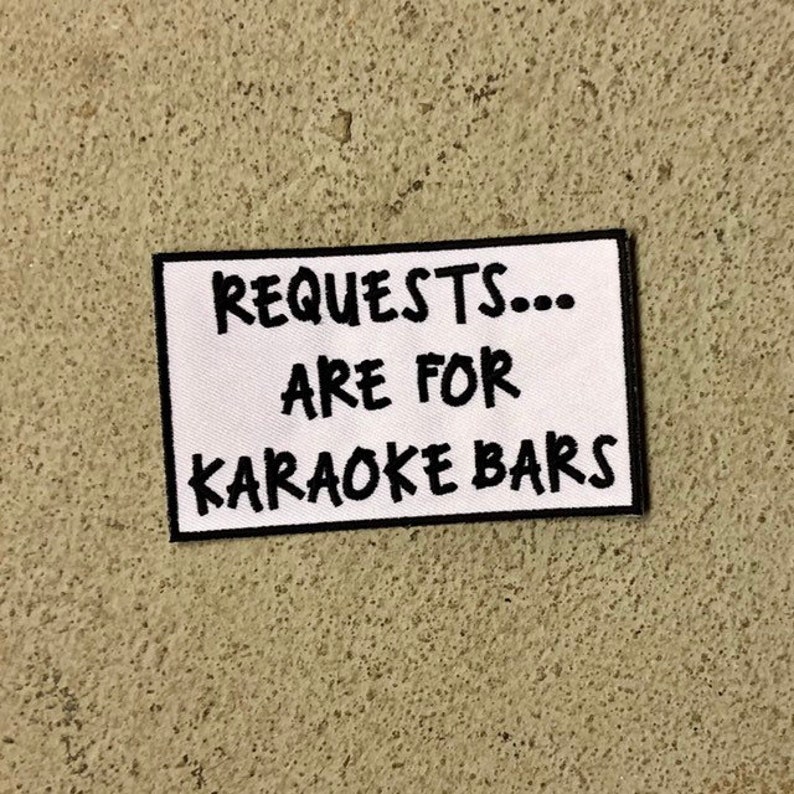 K&ouml;nnte beinhalten: Wei&szlig;er Patch mit schwarzem Text, der "REQUESTS... ARE FOR KARAOKE BARS" lautet.