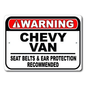 May include: A white warning sign with black and red text. The sign reads "WARNING CHEVY VAN SEAT BELTS & EAR PROTECTION RECOMMENDED".