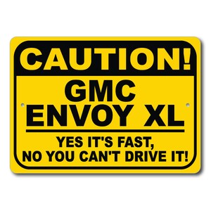 Puede incluir: Un cartel de precaución amarillo y negro con el texto "CAUTION! GMC ENVOY XL YES IT'S FAST, NO YOU CAN'T DRIVE IT!"