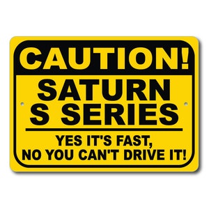 May include: Yellow and black caution sign with the text "CAUTION! SATURN S SERIES YES IT'S FAST, NO YOU CAN'T DRIVE IT!"