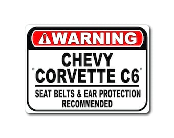 Könnte beinhalten: Ein rechteckiges weißes Schild mit schwarzem Text und rotem Rand. Das Schild lautet "WARNUNG" oben, gefolgt von "CHEVY CORVETTE C6" und "SITZGURTE & GEHÖRSCHUTZ EMPFOHLEN".