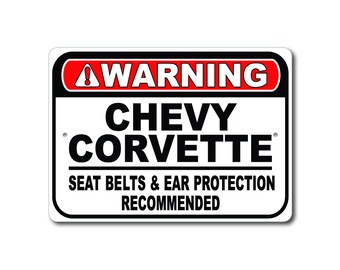 Könnte beinhalten: Ein weißes Warnschild mit schwarzem und rotem Text. Das Schild lautet "WARNING CHEVY CORVETTE SEAT BELTS & EAR PROTECTION RECOMMENDED".