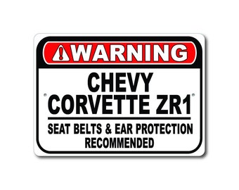 Könnte beinhalten: Ein weißes Warnschild mit schwarzem und rotem Text. Das Schild lautet "WARNING CHEVY CORVETTE ZR1 SEAT BELTS & EAR PROTECTION RECOMMENDED".