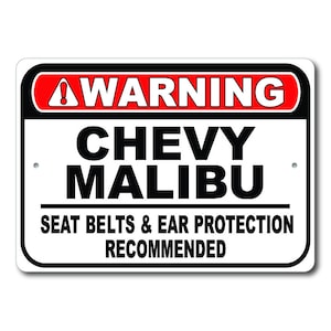 May include: A white warning sign with black and red lettering. The sign reads "WARNING CHEVY MALIBU SEAT BELTS & EAR PROTECTION RECOMMENDED".