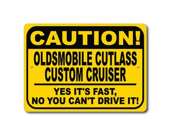 May include: A yellow and black caution sign with the text "CAUTION! OLDSMOBILE CUTLASS CUSTOM CRUISER YES IT'S FAST, NO YOU CAN'T DRIVE IT!"