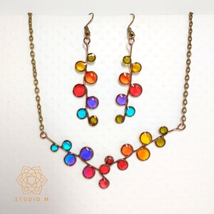 May include: A rainbow colored glass bead necklace and matching earrings. The necklace is a V-shape with a copper wire base. The earrings are long and dangle with a copper wire base.