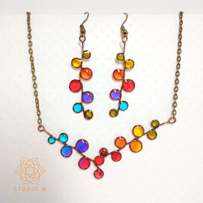 May include: A rainbow colored glass bead necklace and matching earrings. The necklace is a V-shape with a copper wire base. The earrings are long and dangle with a copper wire base.
