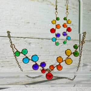 May include: A rainbow colored glass bead necklace and earrings. The necklace is made of a series of connected circles, each a different color of the rainbow. The earrings are a similar design, but smaller.