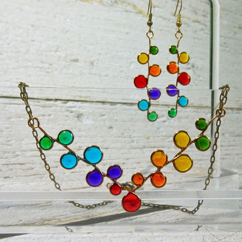 May include: A rainbow colored glass bead necklace and earrings. The necklace is made of a series of connected circles, each a different color of the rainbow. The earrings are a similar design, but smaller.