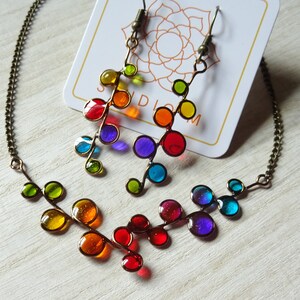 May include: A rainbow colored glass bead necklace and matching earrings. The necklace and earrings are made of small, round glass beads that are strung on a wire. The beads are arranged in a pattern that resembles a branch with leaves. The necklace is approximately 18 inches long and the earrings are approximately 2 inches long.