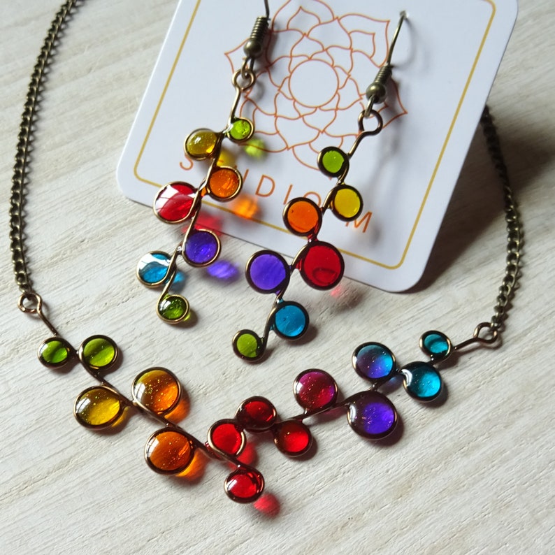 May include: A rainbow colored glass bead necklace and matching earrings. The necklace and earrings are made of small, round glass beads that are strung on a wire. The beads are arranged in a pattern that resembles a branch with leaves. The necklace is approximately 18 inches long and the earrings are approximately 2 inches long.