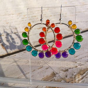 May include: A pair of hoop earrings featuring a silver-toned wire frame adorned with small, translucent, circular beads in a rainbow spectrum of colors including red, orange, yellow, green, blue, and purple, suspended from silver-toned ear hooks.