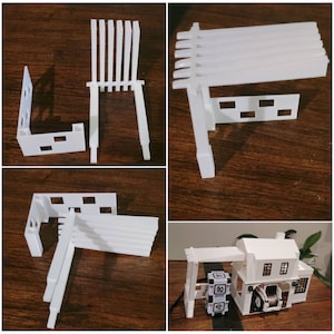 Könnte beinhalten: Ein weißes Plastikmodellhaus mit einer weißen Plastikpergola, einem weißen Plastikstuhl und einem weißen Plastikzaun. Das Haus hat zwei Fenster und eine Tür. Die Pergola ist am Haus befestigt und hat ein Dach. Der Stuhl steht vor dem Haus. Der Zaun ist im Hintergrund.