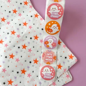 Pode incluir: Um rolo de papel de seda branco com estrelas laranja e pretas impressas. O papel de seda est&aacute; enrolado em torno de um rolo de adesivos com designs fofos de fantasmas. Os adesivos dizem "Stay Spooky", "Cute Stuff Inside" e "Thanks Boo!"