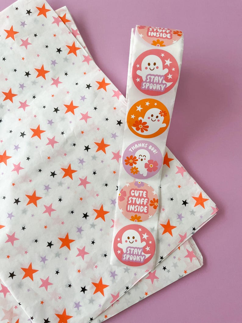 Pode incluir: Um rolo de papel de seda branco com estrelas laranja e pretas impressas. O papel de seda est&aacute; enrolado em torno de um rolo de adesivos com designs fofos de fantasmas. Os adesivos dizem "Stay Spooky", "Cute Stuff Inside" e "Thanks Boo!"