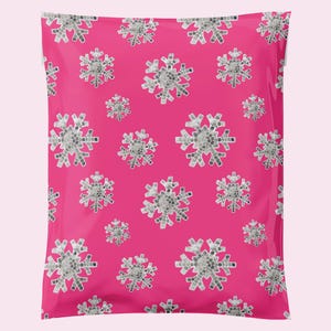 May include: A hot pink shipping mailer bag with a repeating pattern of mosaic-style snowflakes in shades of gray and white. The snowflakes vary in size and are evenly spaced across the surface.