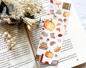 May include: A colorful bookmark with a fall theme. The bookmark features a fox, a pumpkin, a hedgehog, a cup of coffee, books, and leaves. The bookmark is perfect for adding a touch of autumn to your reading.
