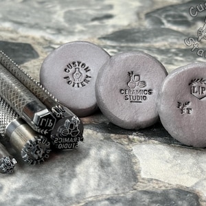 May include: A set of metal stamps for creating custom designs on pottery, ceramics, and other surfaces. The stamps feature various designs, including a hand holding a pot, a vase with flowers, a leaf, and the letters "LP".