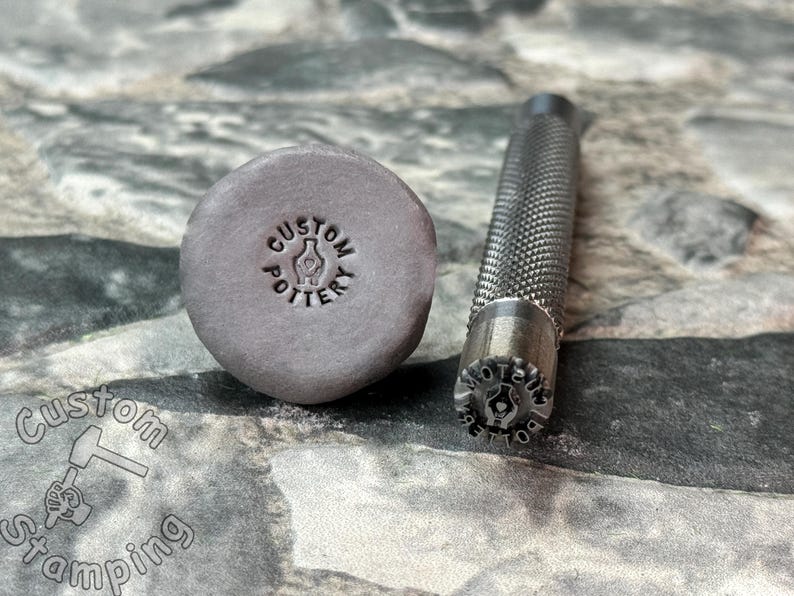 May include: A close-up of a metal stamp with the text "CUSTOM POTTERY" and a hand holding a vase. The stamp is next to a gray clay imprint of the stamp.