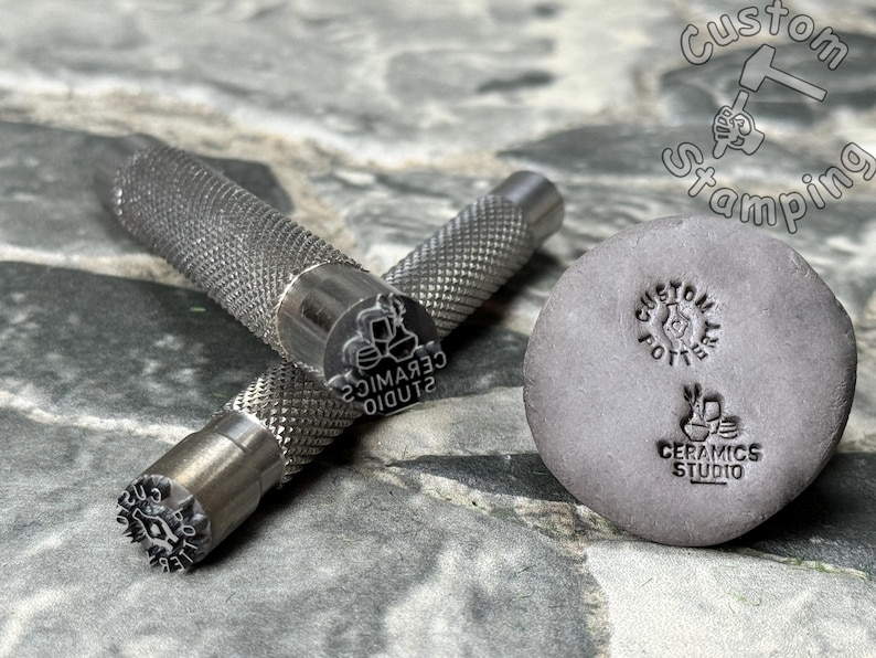 May include: Two metal stamps with handles and a gray clay tile with two impressions. The stamps are engraved with the text "Studio Ceramics" and a design of three ceramic pots. The clay tile has the text "Custom Pottery" and "Studio Ceramics" with a design of a ceramic pot.