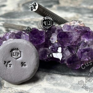 May include: A close-up of three metal stamps with different designs. The stamps are on a bed of purple amethyst crystals. The stamps are used for custom stamping.