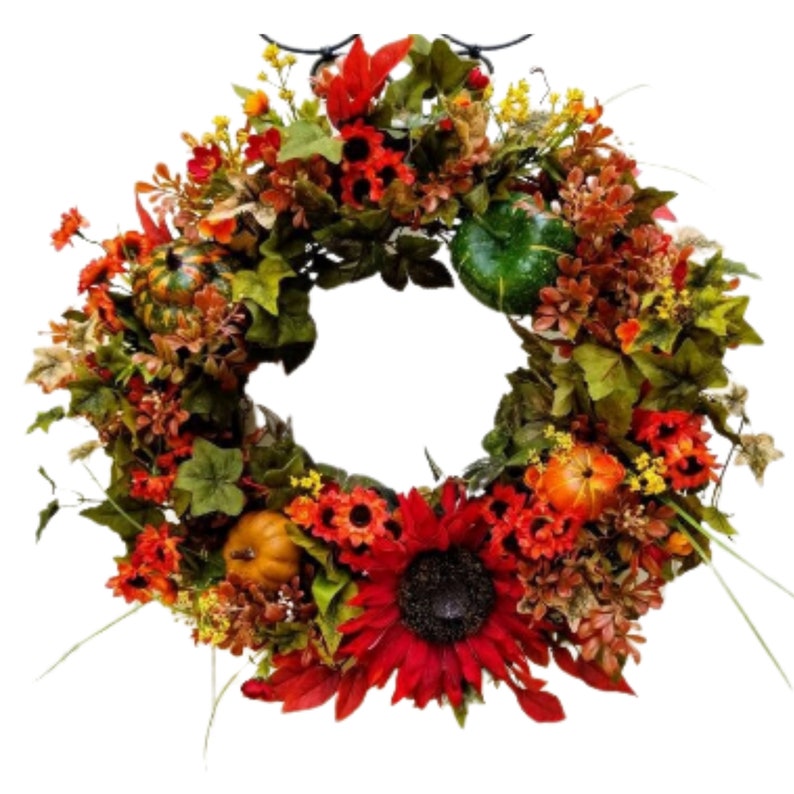 May include: A fall-themed wreath with red, orange, and yellow flowers, green leaves, and small pumpkins. The wreath is decorated with a large sunflower in the center.