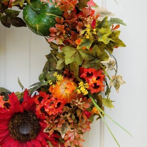 May include: A fall-themed wreath with red sunflowers, orange gourds, and green and brown leaves.