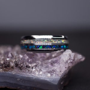 May include: A silver ring with a black band and a blue and white opal inlay. The ring is sitting on a purple amethyst crystal.