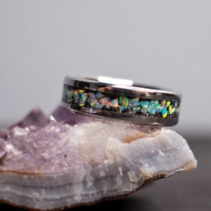 May include: A silver ring with a band of iridescent opal inlay. The ring is sitting on a purple and white crystal.