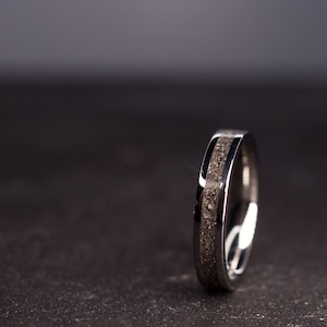 May include: A silver ring with a dark gray inlay. The ring is on a dark gray surface.