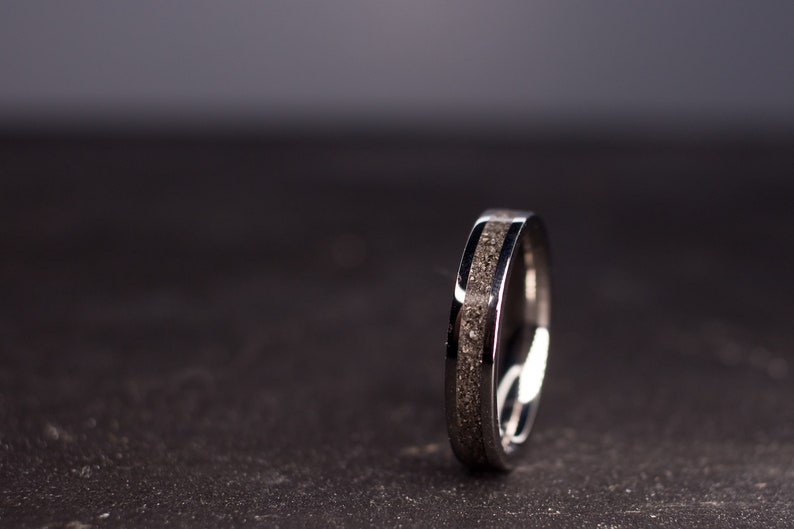 May include: A silver ring with a dark gray inlay. The ring is on a dark gray surface.