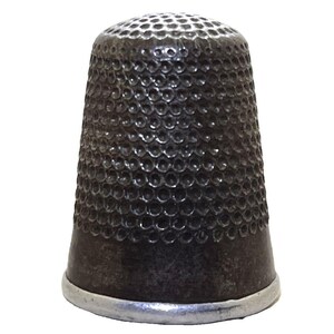 May include: A vintage thimble with a dark, metallic finish. The thimble has a cylindrical shape with a rounded top covered in small, evenly spaced dimples. A silver-colored band encircles the base.