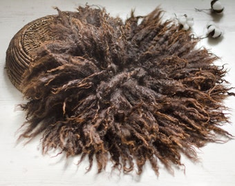 May include: A brown fluffy newborn photography prop made of faux fur. The prop is circular and has a soft, textured appearance.
