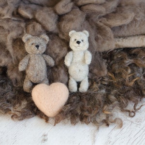 Pu&ograve; includere: Due piccoli orsacchiotti, uno marrone e uno bianco, sono seduti su un letto di pelliccia riccia marrone. Un cuore rosa &egrave; davanti a loro.