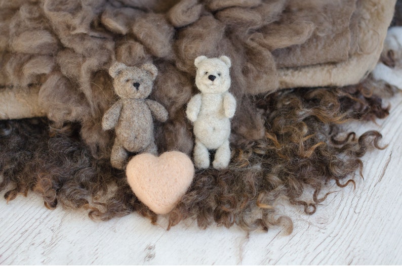 Pu&ograve; includere: Due piccoli orsacchiotti, uno marrone e uno bianco, sono seduti su un letto di pelliccia riccia marrone. Un cuore rosa &egrave; davanti a loro.