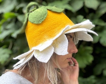 Pode incluir: Um chapéu artesanal em forma de flor amarela com pétalas brancas. O chapéu apresenta folhas e um caule verdes, criando um acessório único. O chapéu é feito de feltro.