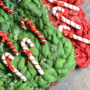 May include: A festive Christmas display featuring green and red woven textures. Candy canes with red and white stripes and red bows are arranged on the textures, creating a seasonal holiday scene.