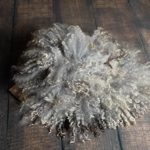 Puede incluir: Una alfombra de piel de oveja gris y blanca esponjosa con un fondo de madera marr&oacute;n.