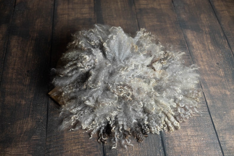 Puede incluir: Una alfombra de piel de oveja gris y blanca esponjosa con un fondo de madera marr&oacute;n.