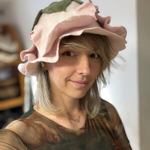 Pode incluir: Um chap&eacute;u artesanal &uacute;nico em forma de rosa rosa grande, com folhas verdes e uma aba com babados. Feito de material de feltro macio, este acess&oacute;rio artesanal &eacute; ideal para fantasias ou eventos especiais, adicionando um toque floral.