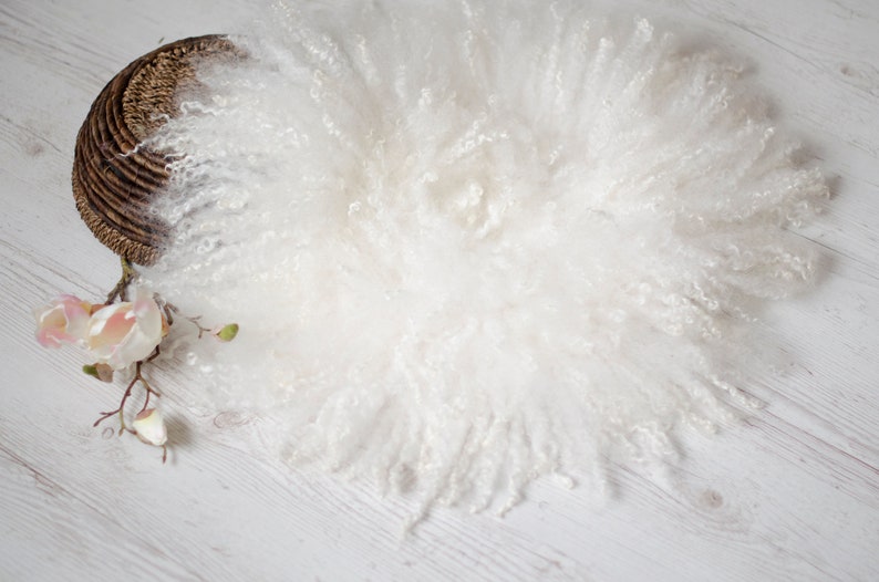 Puede incluir: Alfombra redonda de piel sint&eacute;tica blanca y esponjosa sobre un fondo de madera blanca. La alfombra es redonda y tiene una textura suave y esponjosa.